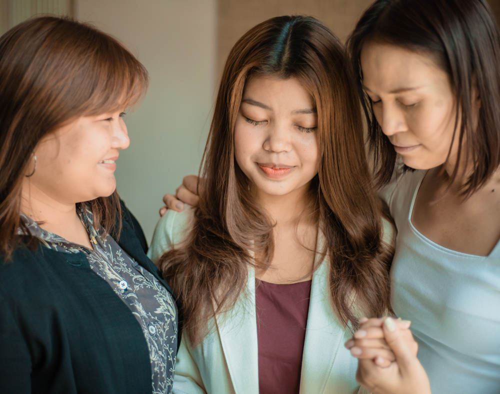 Tres personas de apariencia femenina mirando algo juntas, apoyándose mutuamente. 