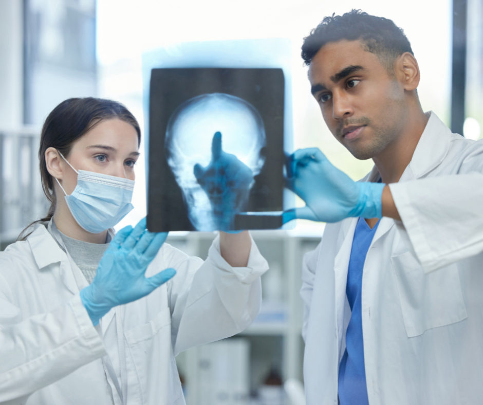 Dos personas con batas de laboratorio mirando una radiografía de un cráneo. 