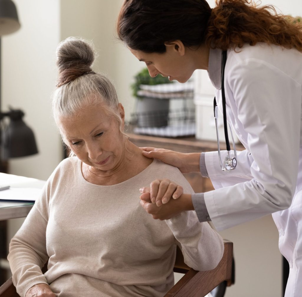 Mujer médico inclinándose para consolar a un paciente sentado. 